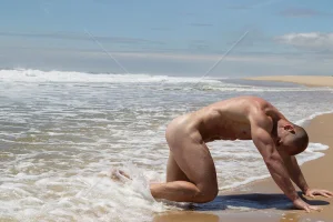 naked-bodybuilder-on-his-hands-and-knees-at-the-ocean.webp